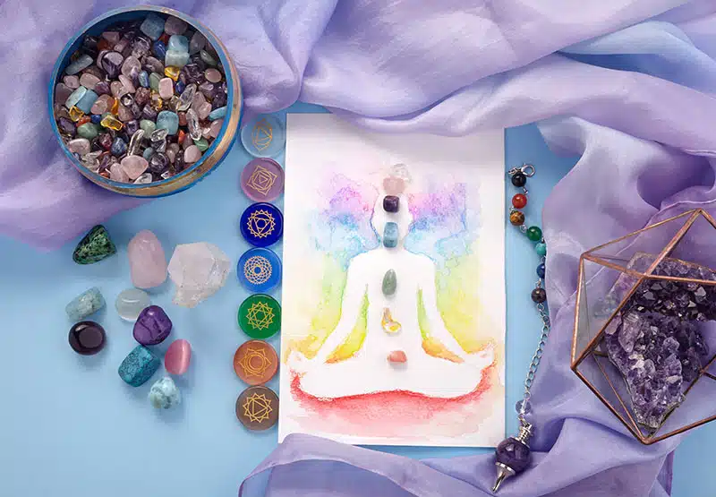 reiki-ausbildung-800 eine Karte mit einer Chakra-Zeichnung, umgeben von Chakrensteinen und einem fliederfarbenen Tuch und anderen Edelsteinen